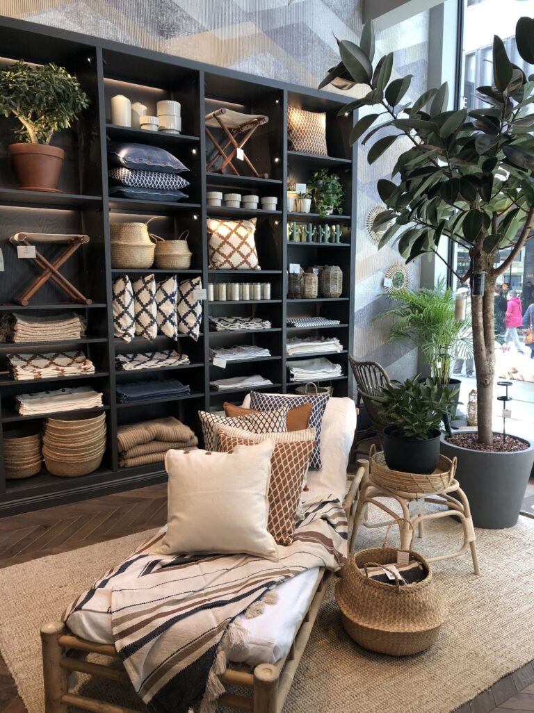 Boutique déco avec étagères noires organisées, textiles naturels et coussins géométriques. Ambiance zen et chaleureuse inspirante pour Home Organizer Nantes. Aménagement style naturel par HO BLANDINE, professionnelle du rangement.