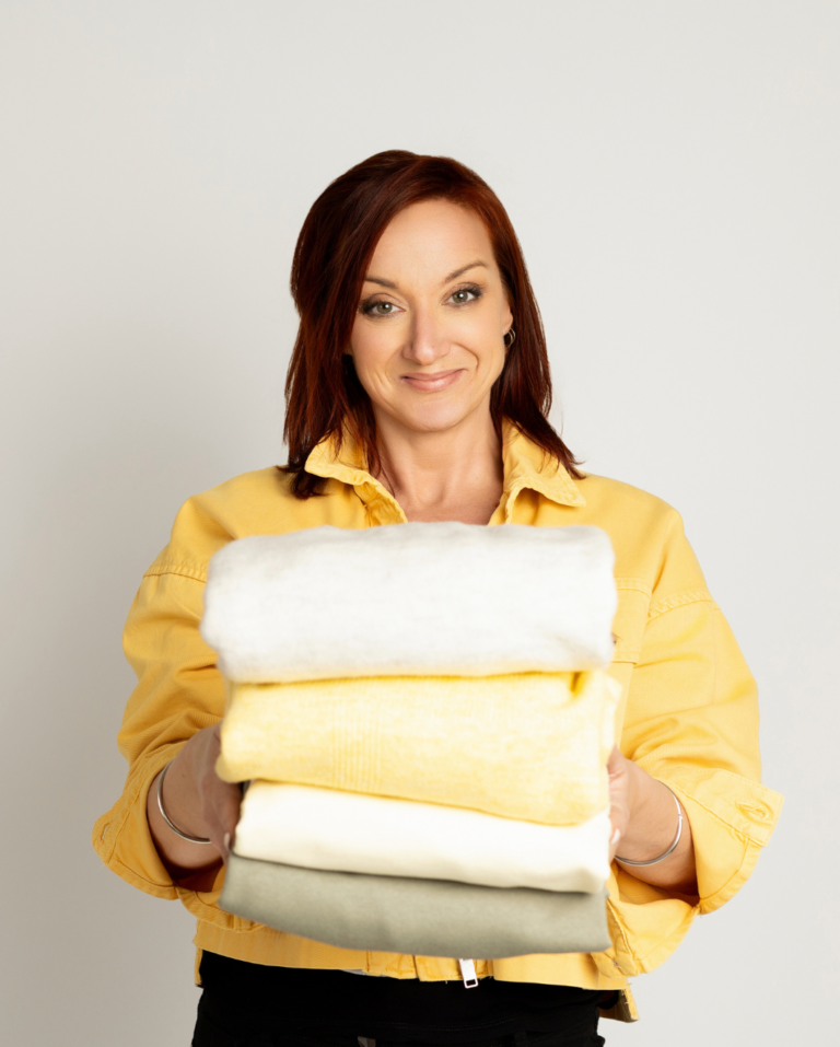 Portrait professionnel de Home Organizer Nantes présentant des textiles parfaitement pliés en blanc, jaune et beige. Image de HO BLANDINE en veste jaune soleil illustrant l'expertise du rangement et du pliage, symbolisant l'harmonie et l'organisation représentée dans les intérieurs.
